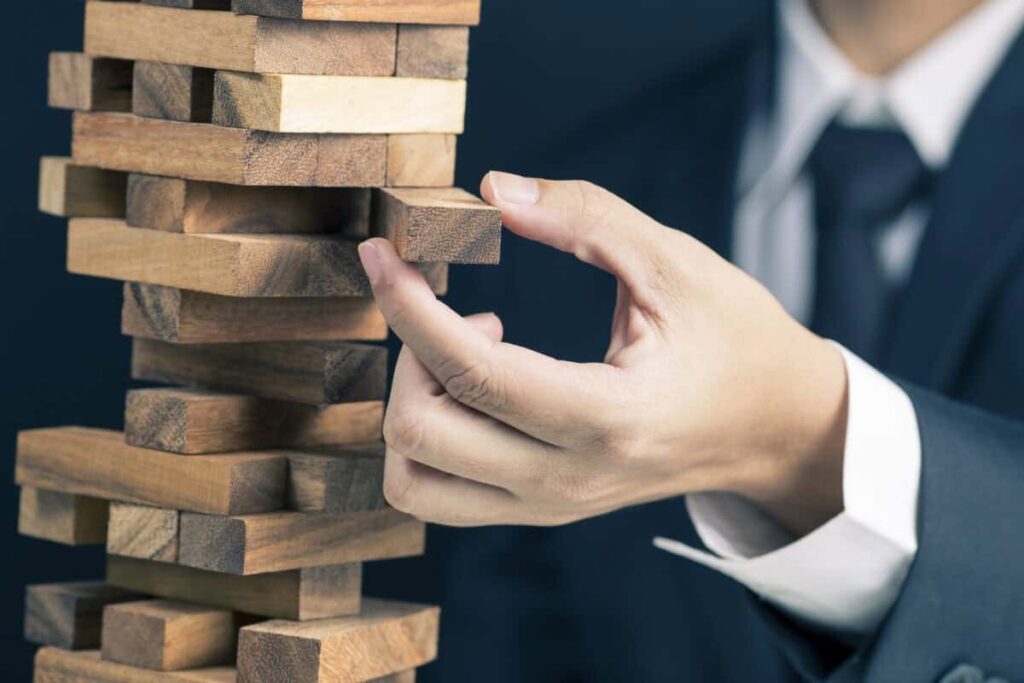 2 Undervalued Canadian Stocks Primed for Big Returns man in business suit pulls a piece out of wobbly wooden tower